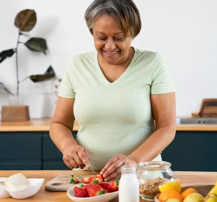 A smiling woman cutting strawberries at a kitchen counter full of fruit