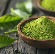 A wooden bowl of bright green leaf powder beside fresh leaves, a stock photo from the brand's image set