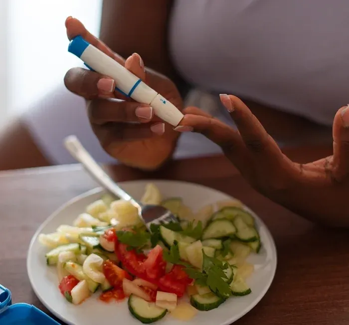 A person using a finger-prick lancet next to a plate of salad
