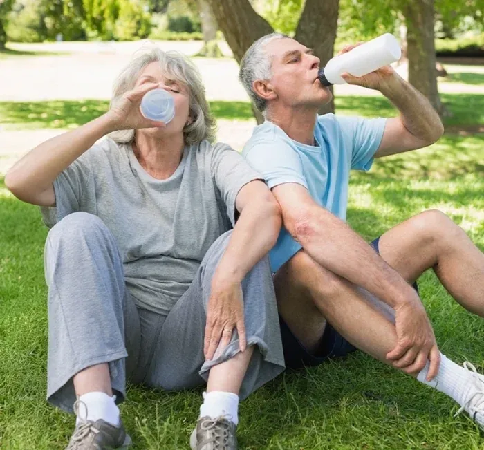 An older couple drinking water while resting on grass