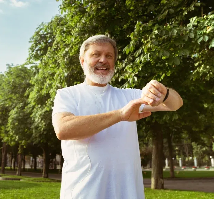 A smiling man in a park checking his watch